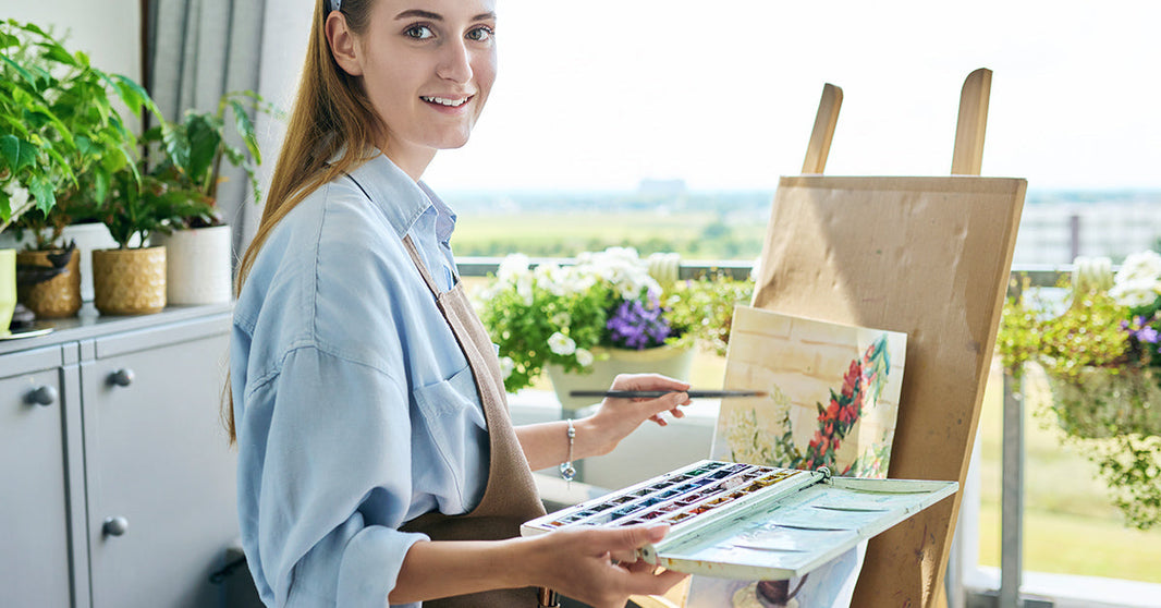 Frau malt mit Aquarellpinseln an einer Leinwand ein Aquarell